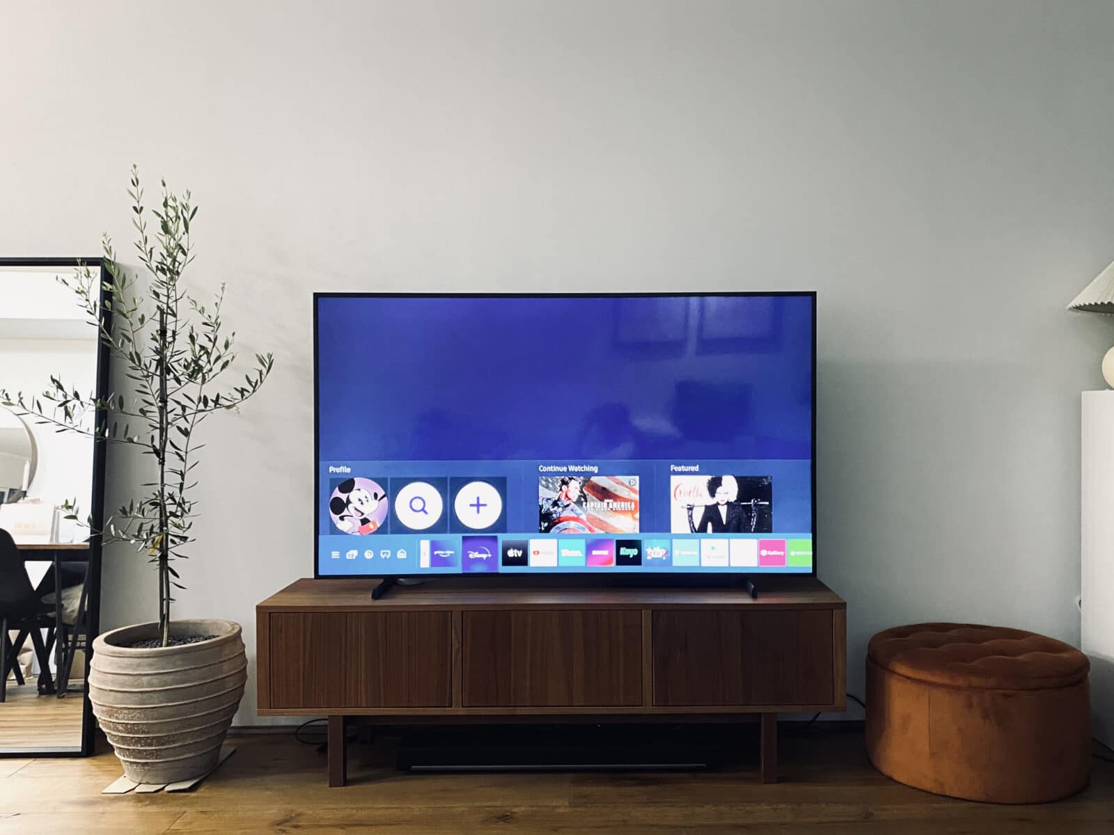 65-inch Samsung Frame TV 2021 model on a brown wood entertainment unit displaying the Home Screen
