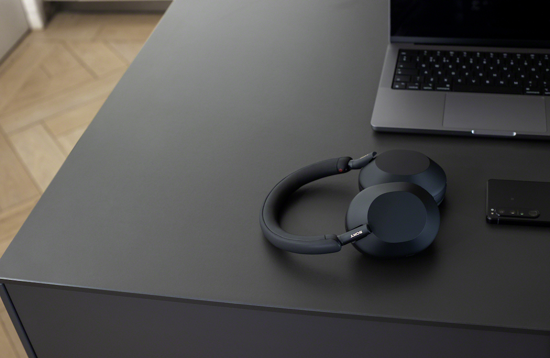Sony WH-1000XM5 in black on a black table next to a laptop